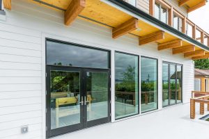 Waterfront Magnolia home with new decking, railings, large windows, and exterior doors integrated into a fully rebuilt siding and waterproofing system.