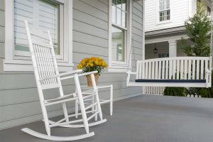 The front porch of a home with a white rocking chair and a white porch swing