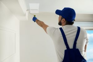 A handyman painting a ceiling with white paint.