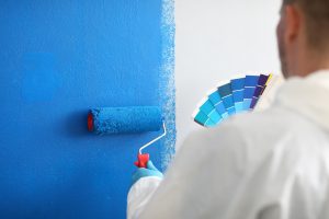 Craftsman holds roller and a blue color palette and paints a white wall blue. 