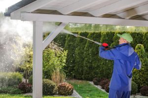 A contractor power-washing a patio cover in a backyard