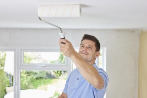 Man Painting Ceiling In Room Of House With Paint Roller