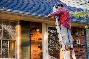 Man Cleaning Gutters on a Ladder Against a Brick House