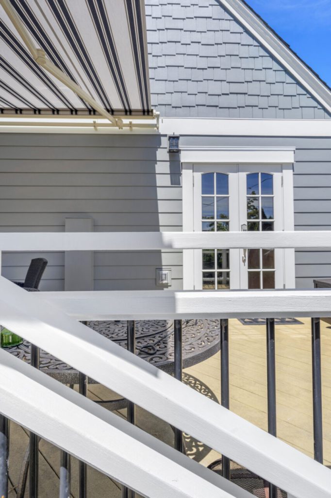 Close-up of Green Lake Seattle home showing new deck railing, Hardie plank siding, wood shingle accents, updated trim, and exterior door following full exterior rebuild.