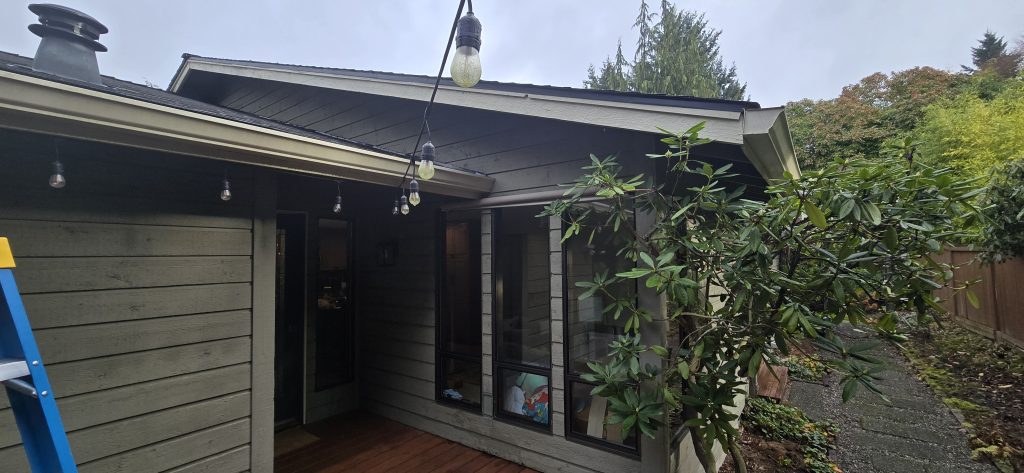 Lake Forest Park home with leaking cedar channel siding and water damage below gutter end; visible moisture intrusion at roof-to-wall connection.