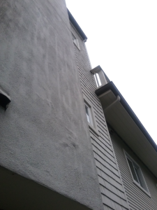 Stucco wall showing early cracking and surface distress near siding transition, a common source of water intrusion requiring stucco crack repair in Seattle-area buildings.